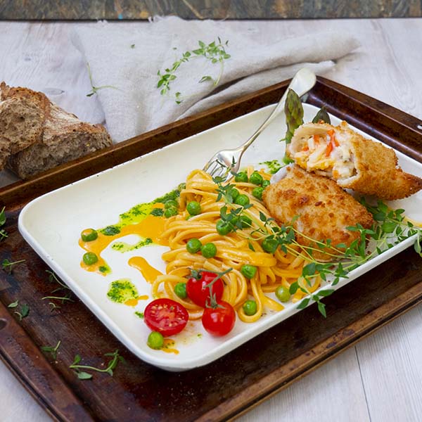 Sprøbakt fiskerullade Julienne anrettet på tallerken med pasta i skalldyrsaus, erter og cherrytomat