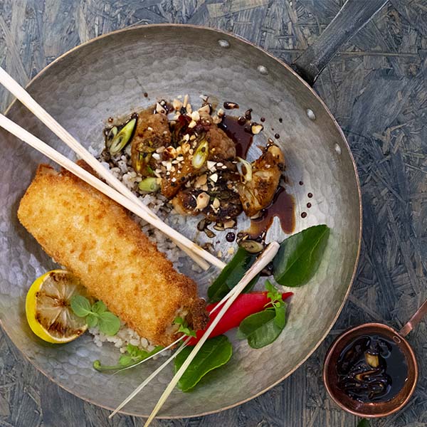 Sprøbakt fiskerullade på tallerken med stekt blomkål i teriyaki-saus, drysset med ristede cashewnøtter 